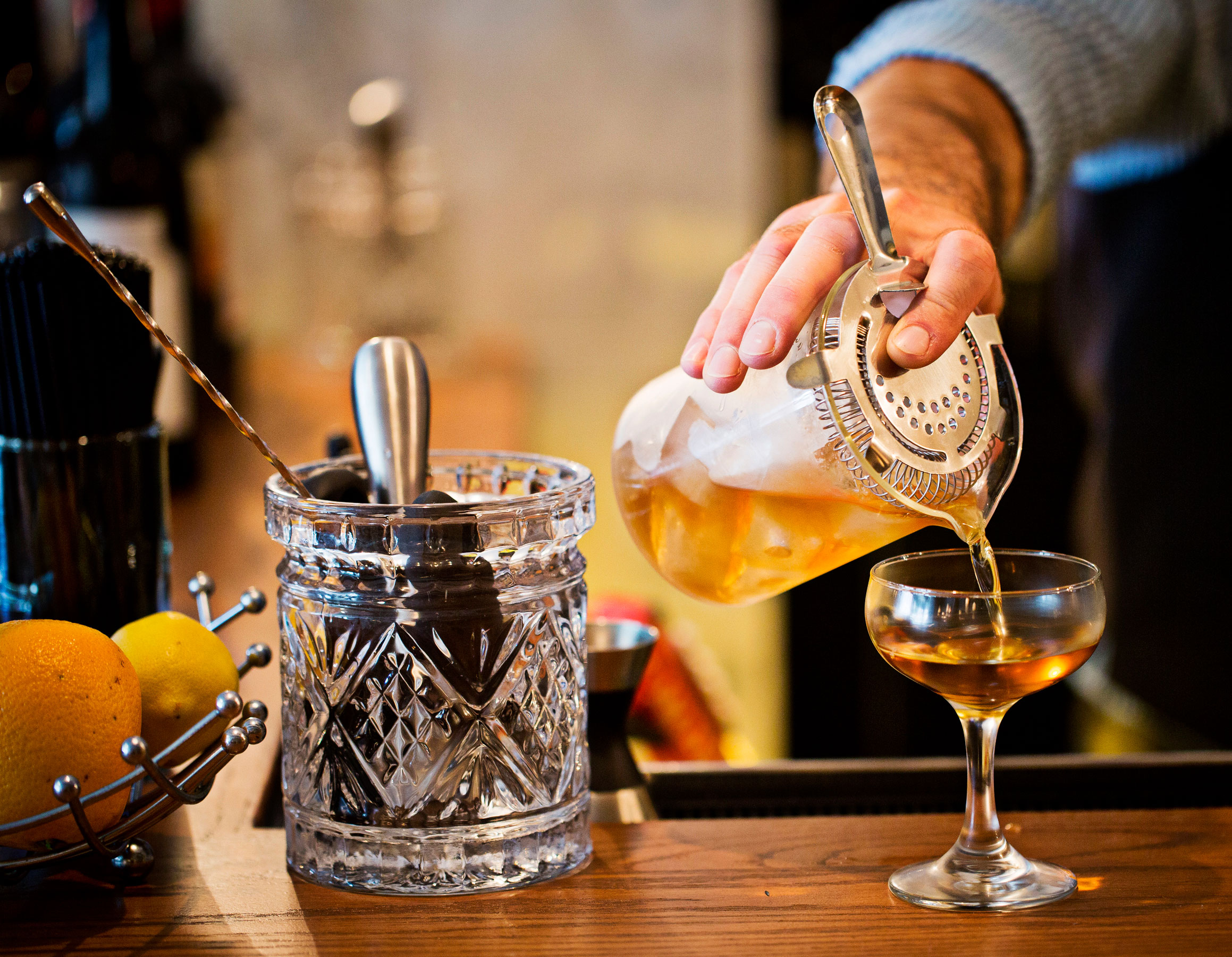 bartender pouring a craft cocktail into a glass