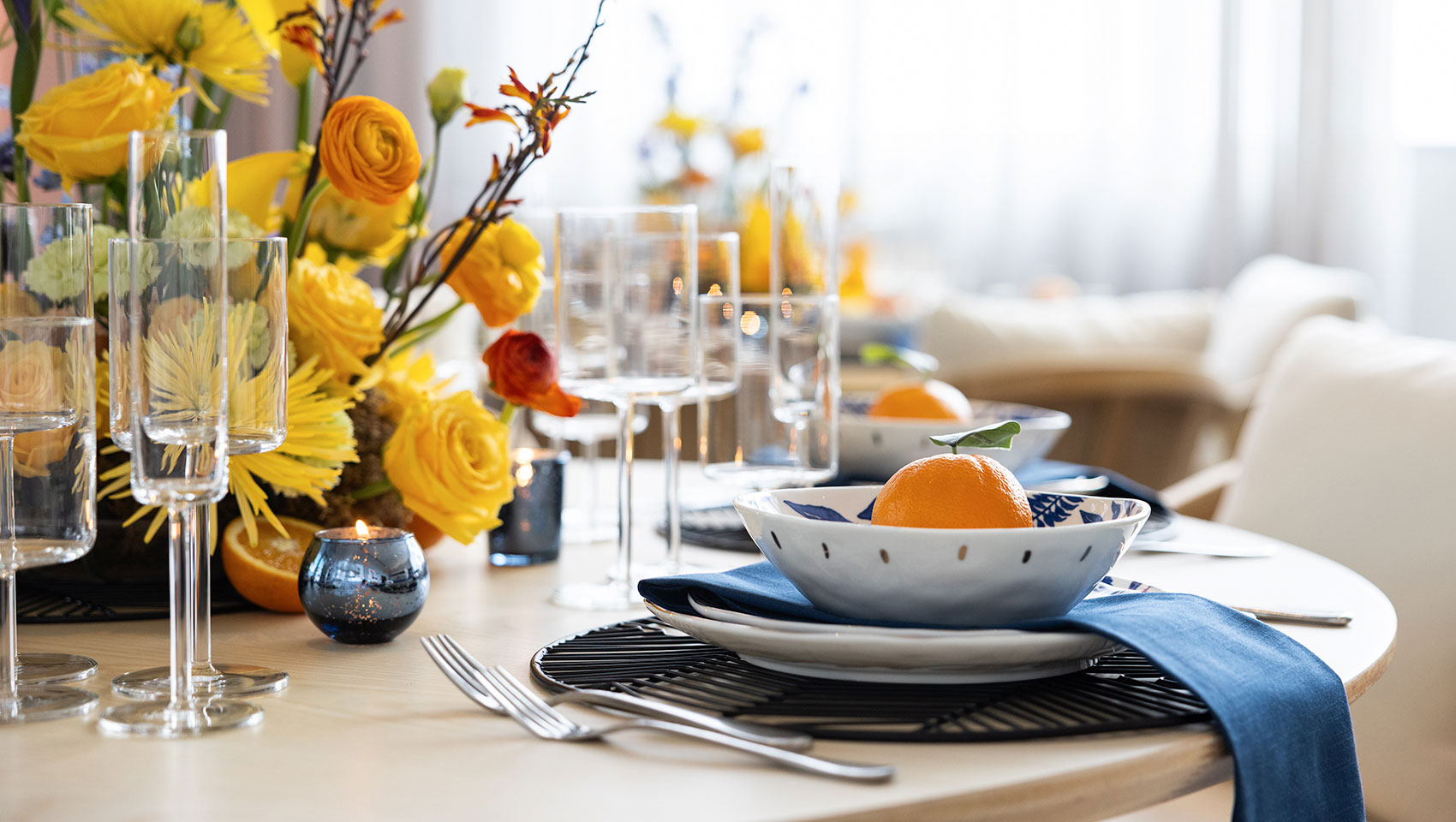 Fresco Room Social Set Up Table with flowers, blue napkins, candles, as well as an orange in a bowl