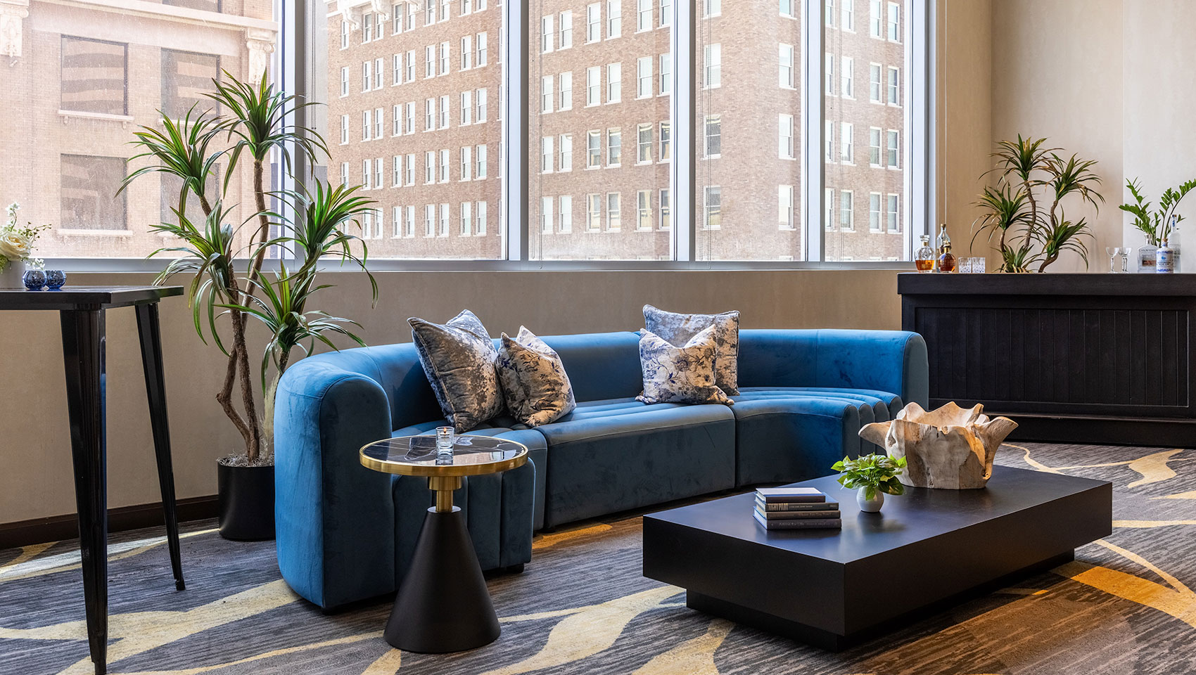 Mural Room Lounge and Bar Set-up with blue sofa, side table with candle, coffee table with books, plant and sculpture